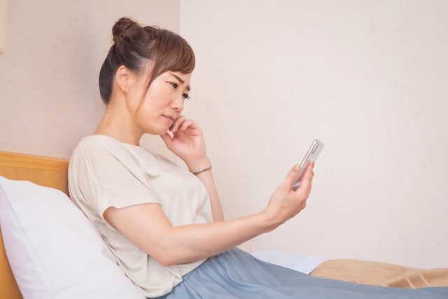 スマホを見ながら悩む女性